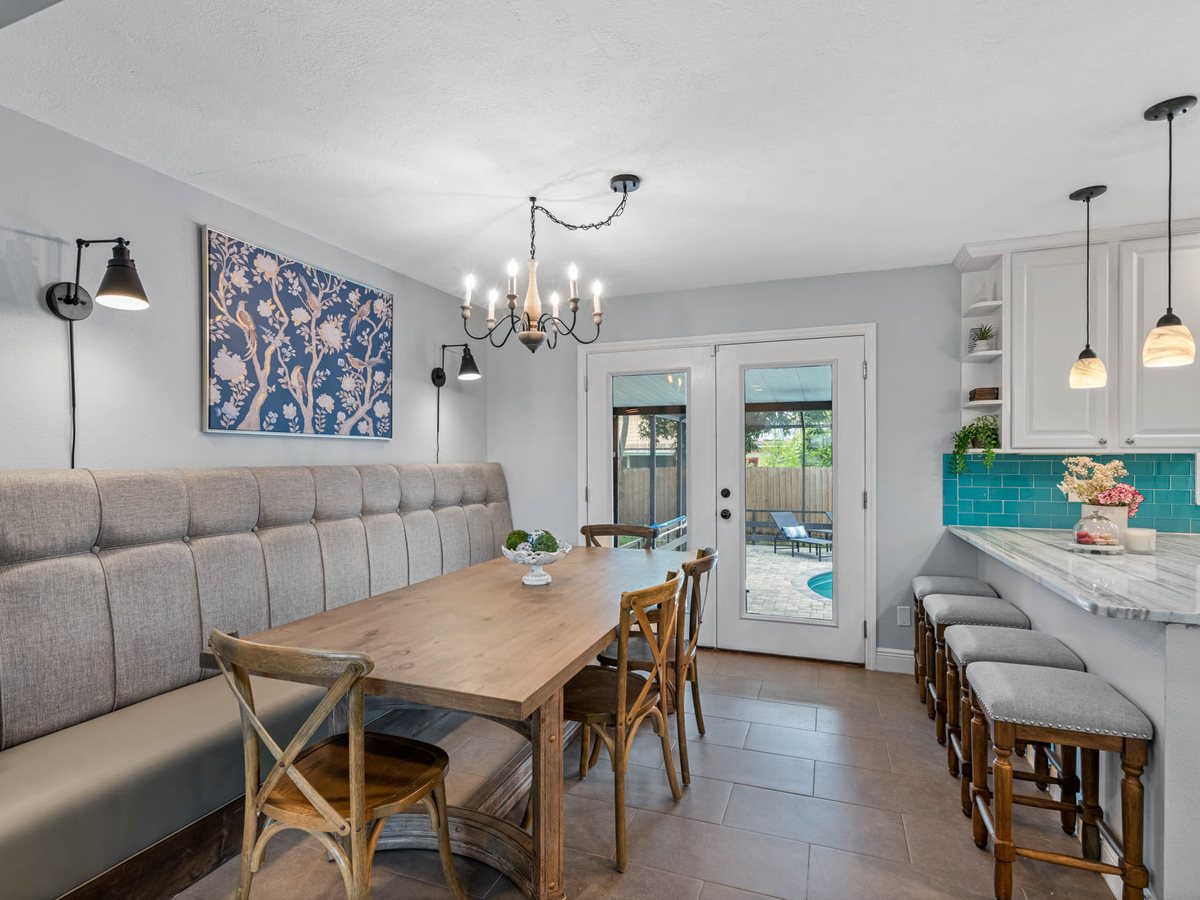 Dining room with a tufted banquette, wooden chandelier and a teal tile backsplash beyond